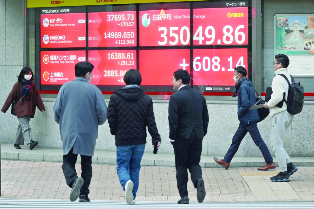 Pedestrians walk past a signboard showing the closing numbers on the Tokyo Stock Exchange, along a street in Tokyo. - AFP
 