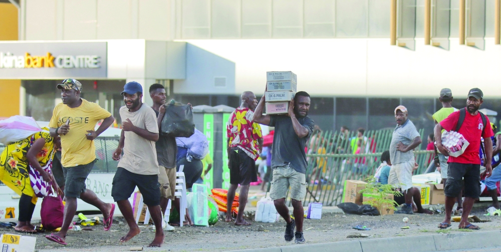 People carry looted goods amid a state of unrest in Port Moresby. — AFP