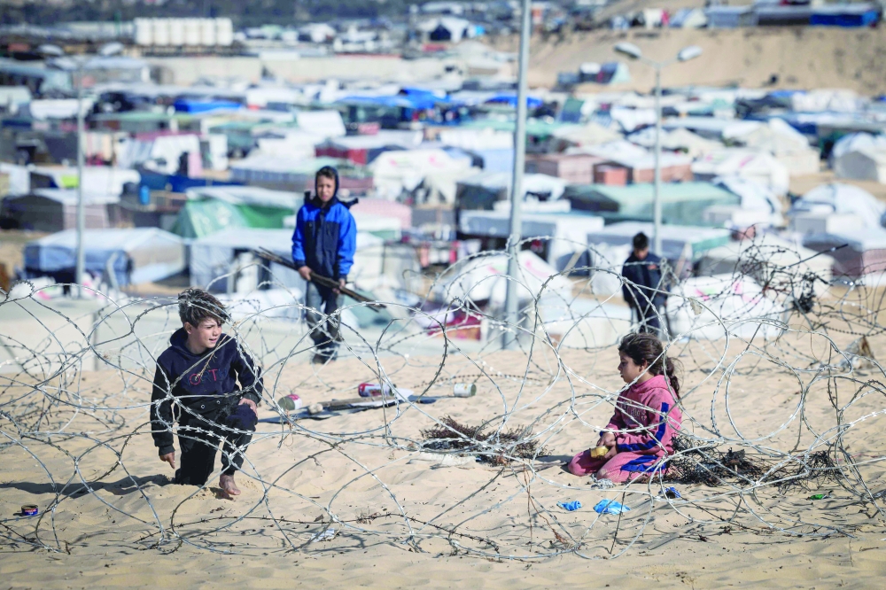 Displaced Palestinian play behind barbed wire on a sand dune overlooking a makeshift camp, west of Rafah. — AFP