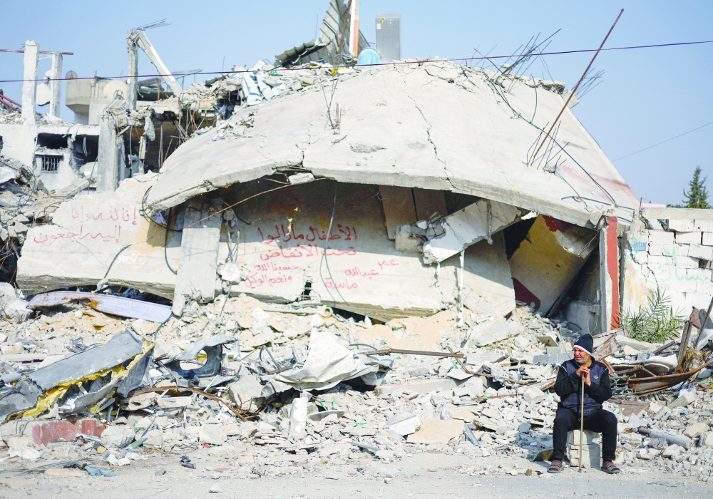 A man sits next to writing painted on a wall amid the rubble of a house, which was destroyed in a deadly Israeli strike, in Rafah. — Reuters 