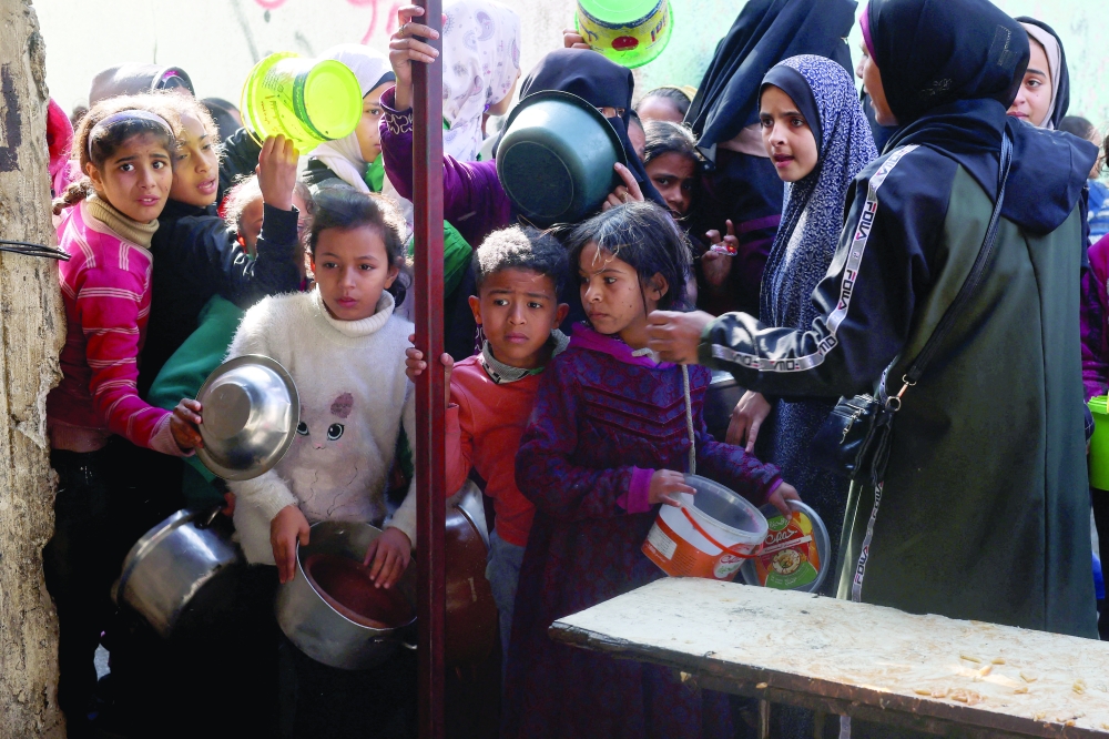 Palestinians wait to receive food cooked by a charity kitchen amid shortages of food supplies, in Rafah. — Reuters