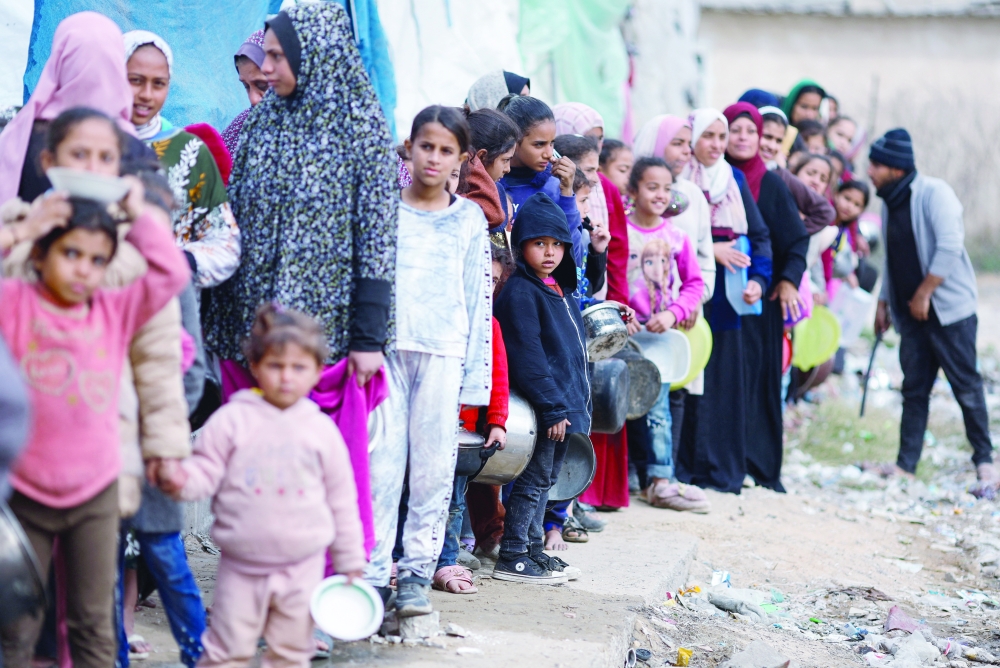 Palestinians stand in a line as they wait to receive food amid shortages of food supplies, in Rafah. — Reuters