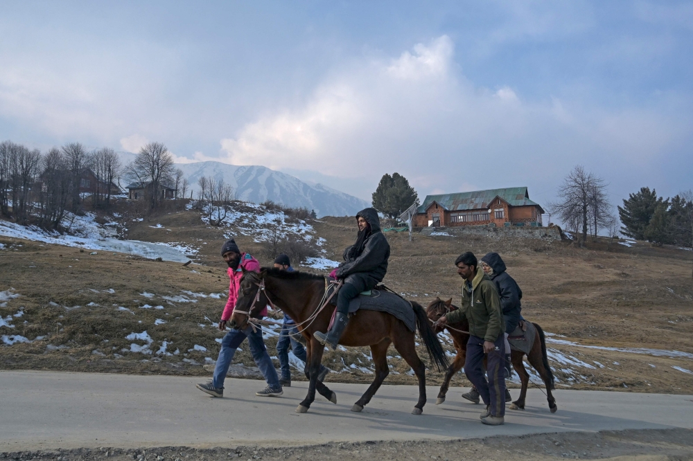 Guides lead visitors during a horse ride past ski slopes usually covered in snow at this time of the year at a ski station in Gulmarg