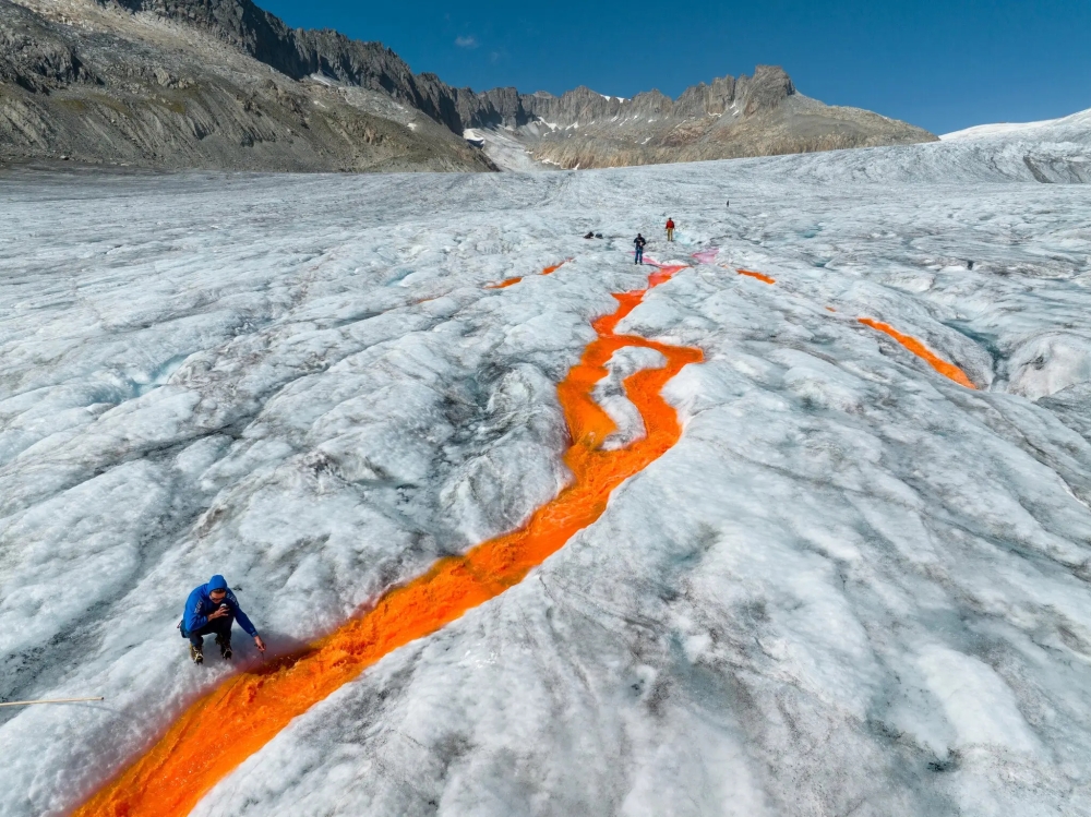 Graduate students from ETH Zurich use orange dye to track and measure surface melt at the Rhône Glacier, which has retreated about half a kilometer since 2007.
