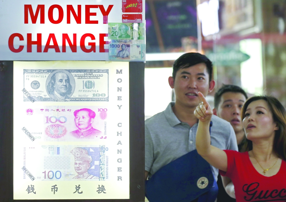People look at the exchange rate at a money changer displaying posters of US dollars, Chinese Yuan and Malaysia Ringgit in Singapore. — Reuters
