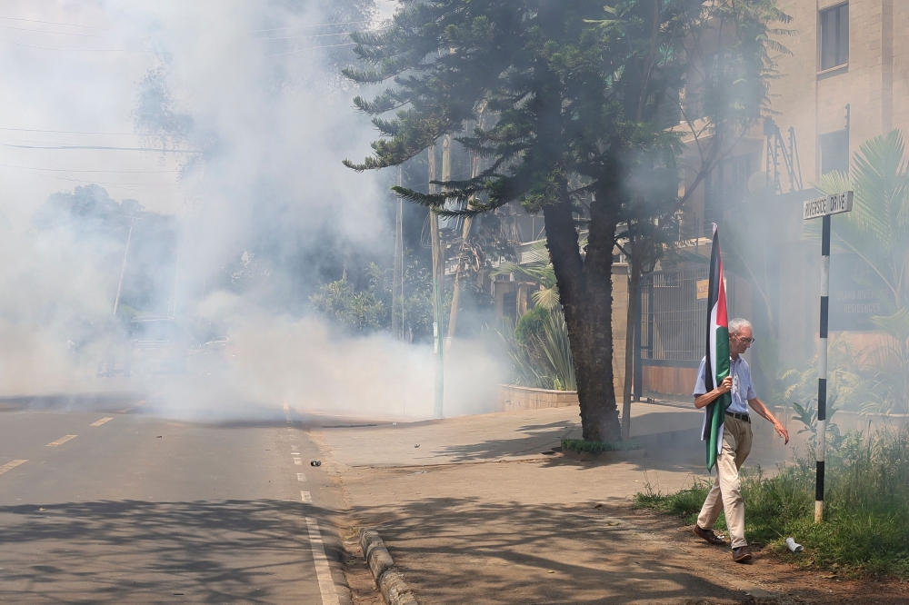 A pro-Palestinian supporter carrying a Palestinian flag walks away from teargas during a demonstration outside the German embassy in Nairobi