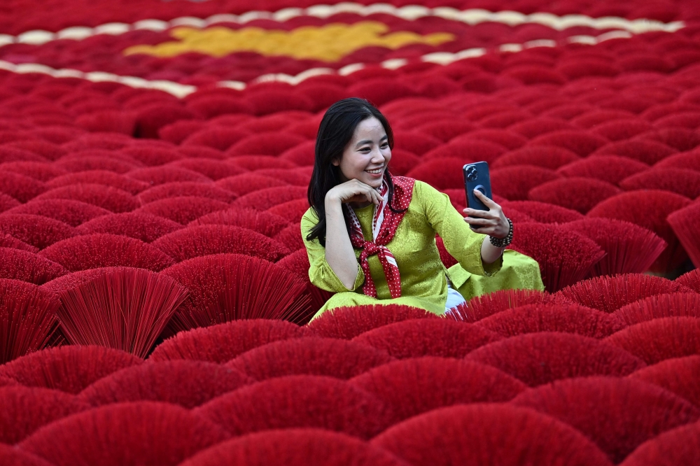A tourist takes a selfie picture in front of incense sticks arranged in the form of a Vietnamese flag in a courtyard in the village of Quang Phu Cau on the outskirts of Hanoi. - AFP