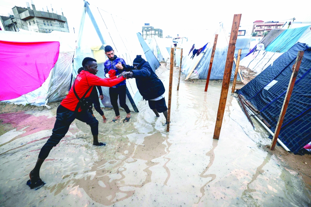 A Displaced Palestinians man helps a woman to find her way amid tents flooded by heavy rain, at a makeshift camp set up by people who fled the ongoing battles, in Rafah. — AFP 