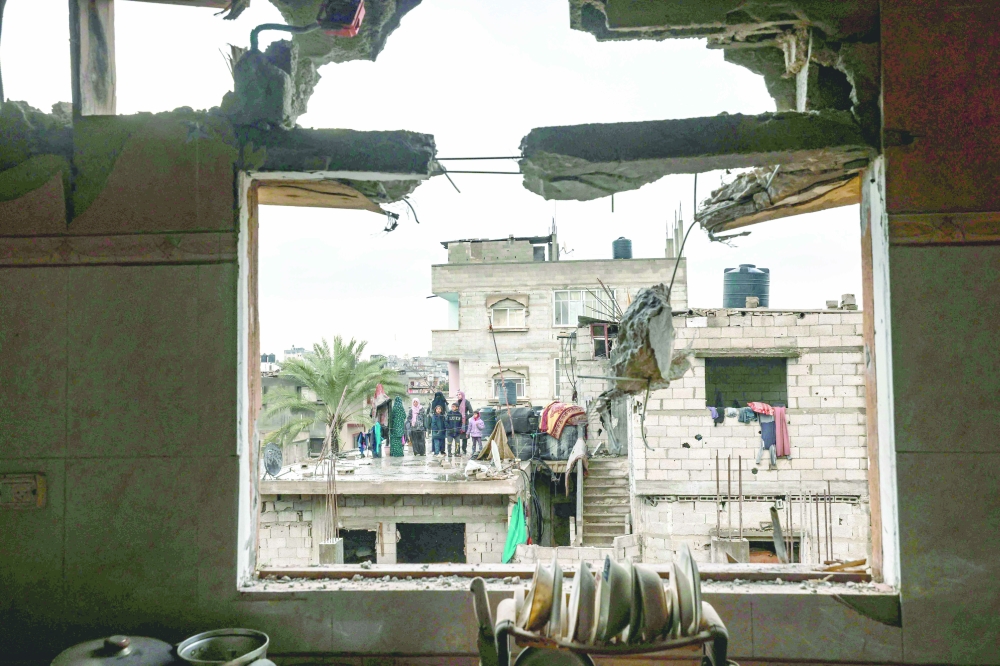 A picture taken through the window of a building damaged by Israeli bombing, shows members of a family standing on a rooftop, in Rafah in the southern Gaza Strip. — AFP