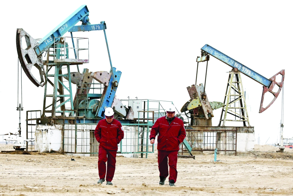 Workers walk as oil pumps are seen in the background in the Uzen oil and gas field in the Mangistau Region.__REUTERS