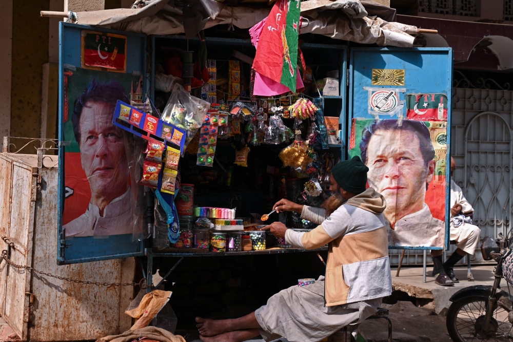 A vendor sits at his tuck shop displaying posters of Pakistan's former Prime Minister and Pakistan Tehreek-e-Insaf (PTI) leader Imran Khan