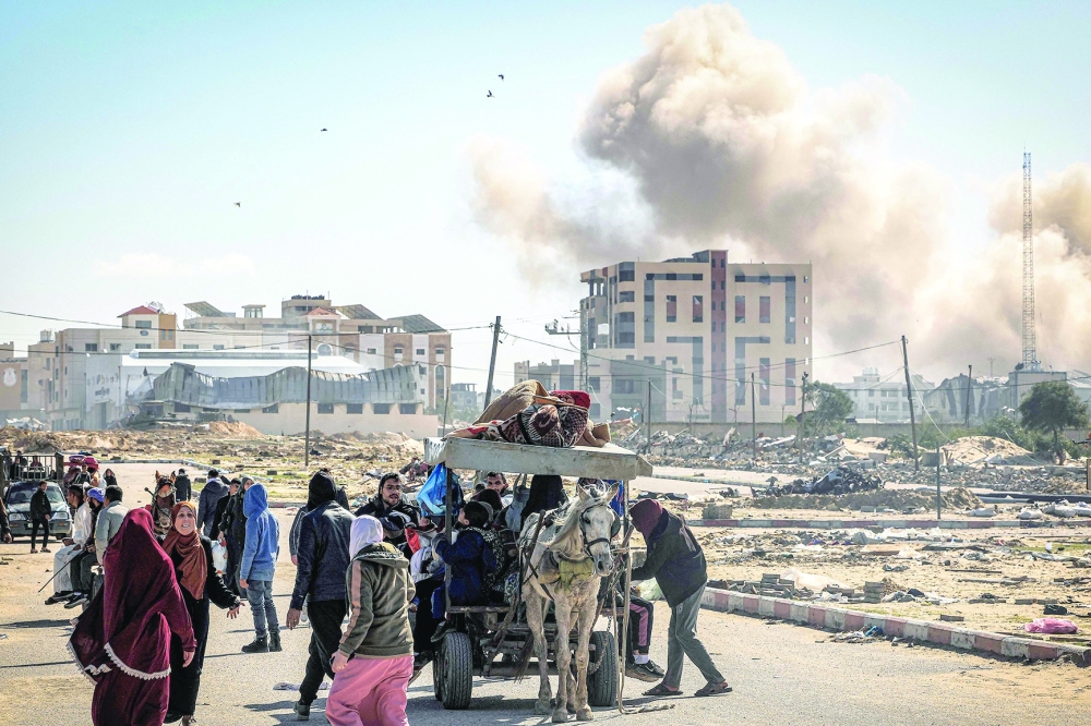 Smoke from bombardment billows in the background as displaced Palestinians flee from Khan Yunis. — AFP