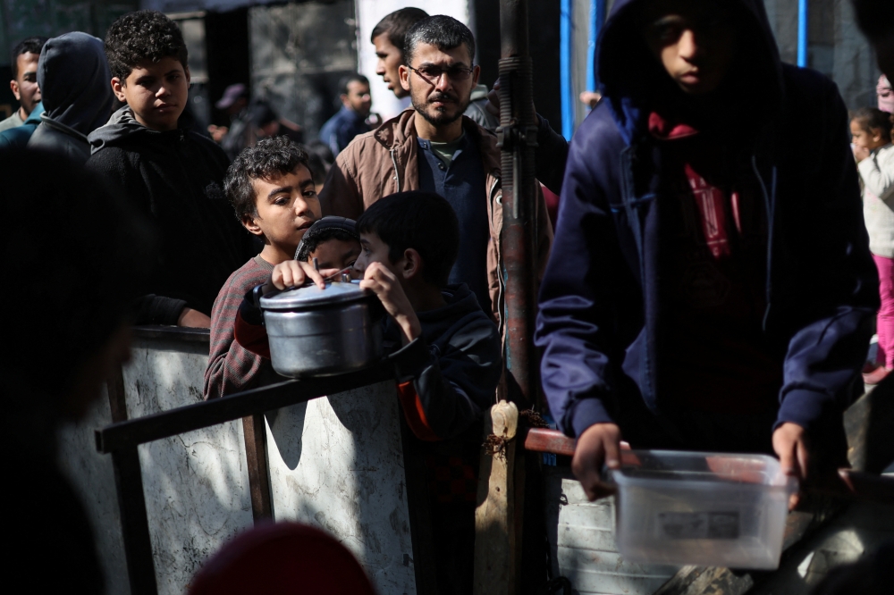 Palestinians wait to receive food cooked by a charity kitchen amid shortages of food supplies, in Rafah. — Reuters 