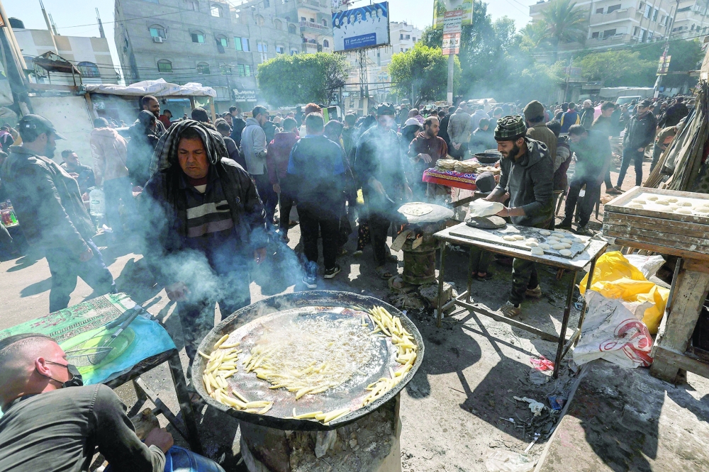 Vendors prepare bread and fry potatoes for sale as street food along a crowded main street in Rafah, in southern Gaza Strip. - AFP
