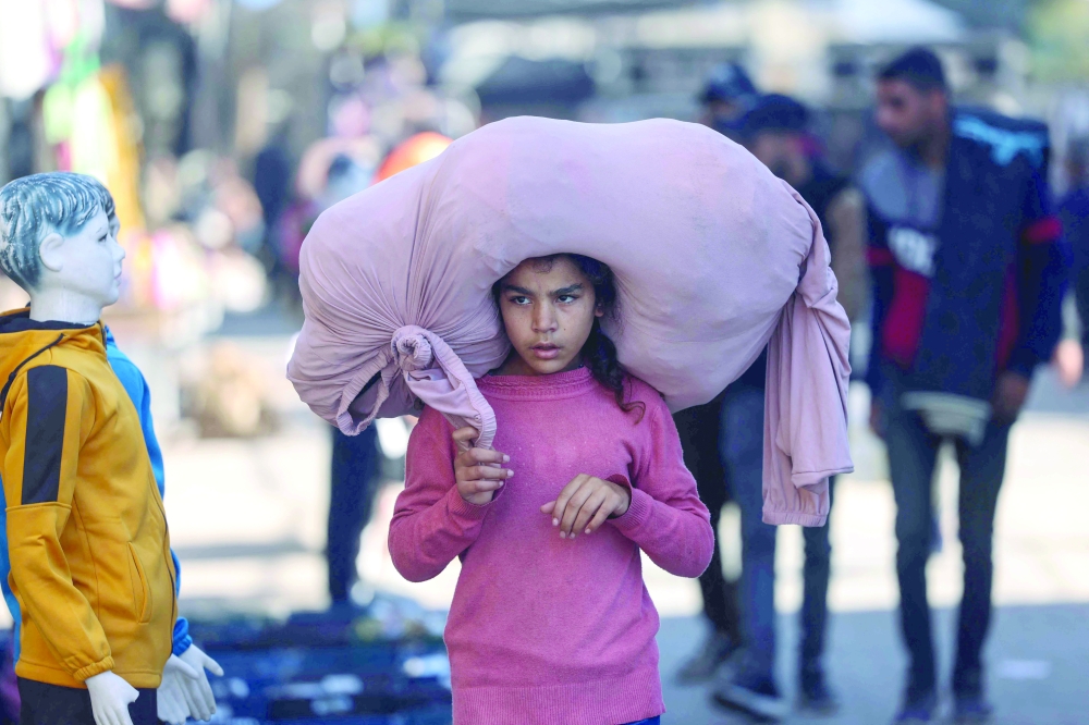 A Palestinian girl walks while carrying a bundle on her head on a busy street in Rafah in the southern Gaza Strip on Sunday. — AFP
