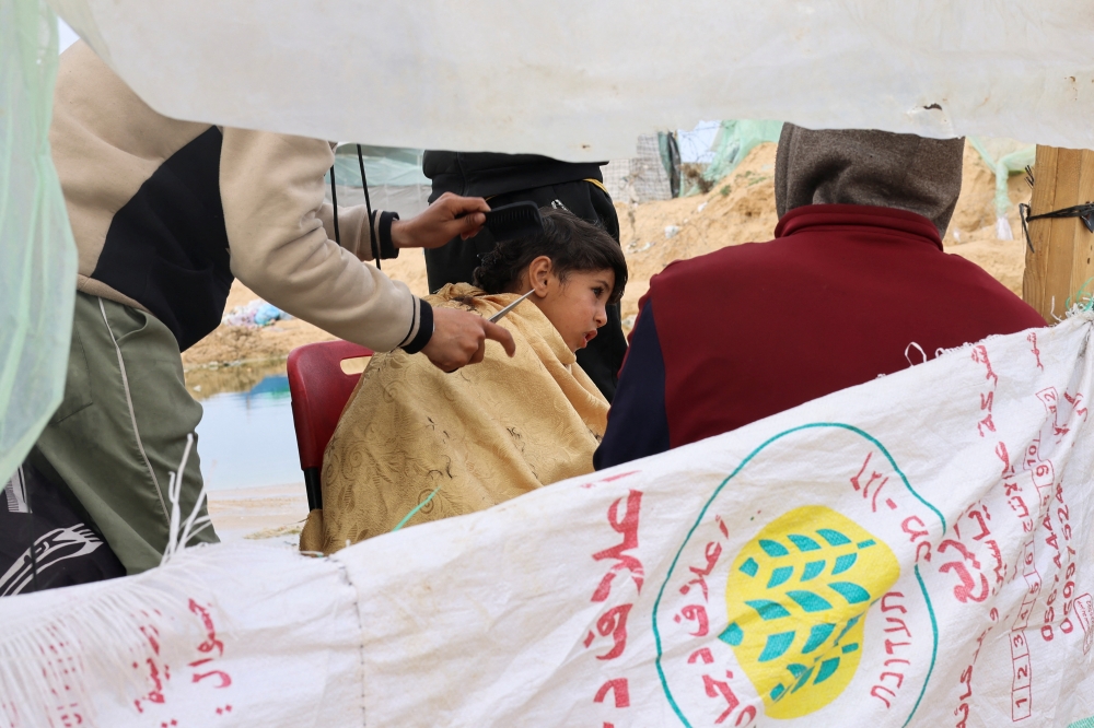 A displaced Palestinian boy gets a haircut at a tent camp