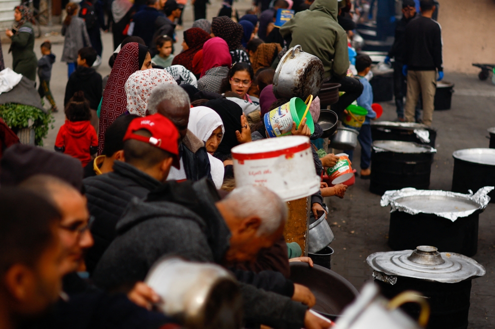 Palestinians wait to receive food cooked by a charity kitchen amid shortages of food supplies
