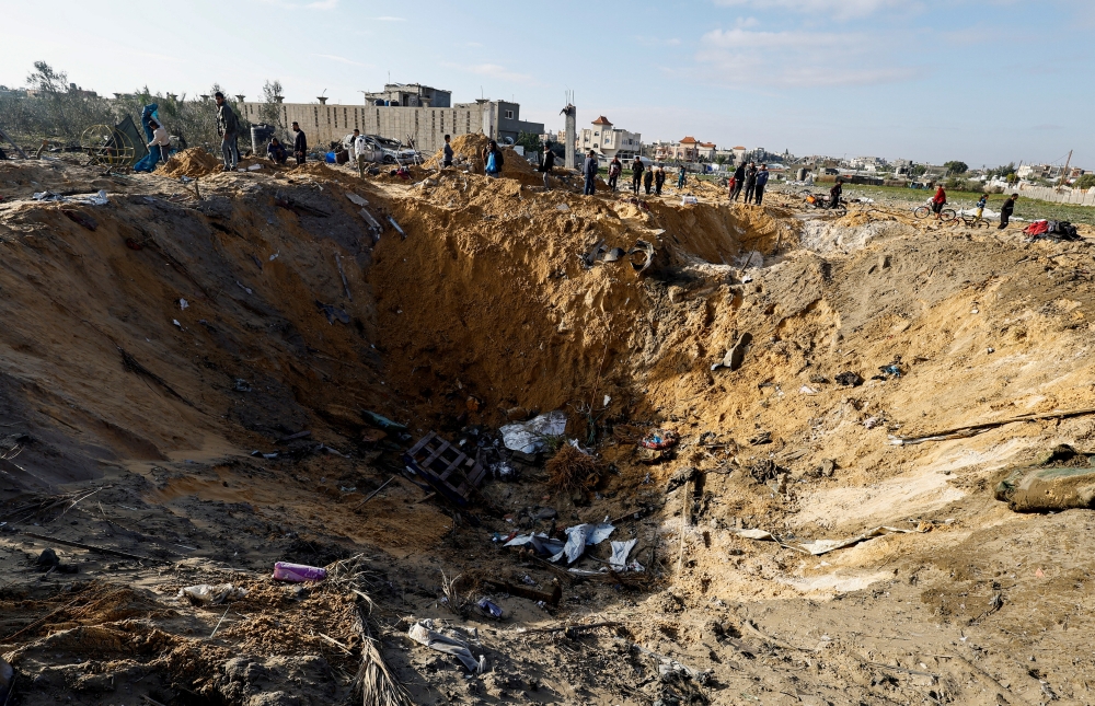 Palestinians gather near a crater at the site of an Israeli strike on a house, amid the ongoing conflict between Israel and Palestinian Islamist group Hamas, in Rafah, in the southern Gaza Strip, February 18, 2024. 
