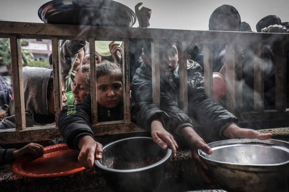 TOPSHOT - Displaced Palestinian children gather to receive food at a government school in Rafah in the southern Gaza Strip on February 19, 2024, amid the ongoing battles between Israel and the militant group Hamas. (Photo by MOHAMMED ABED / AFP)

