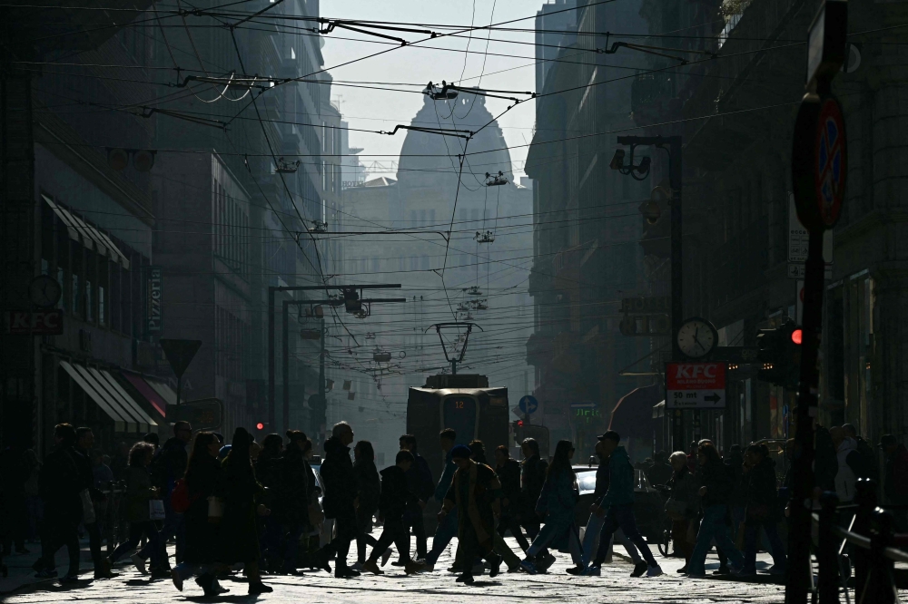 People cross a busy street in Milan's city center on February 20, 2024. Gas-guzzling cars were banned from roads Tuesday in Milan and eight other cities across Lombardy after the northern Italian industrial region registered high levels of particle pollution dangerous for health. (Photo by GABRIEL BOUYS / AFP)


