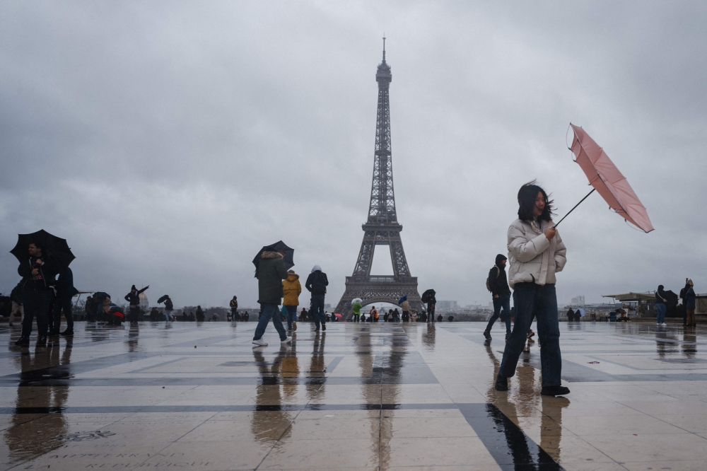 A tourist tries to protect herself with an umbrella on a rainy day at the Esplanade du Trocadero with the Eiffel Tower in the background