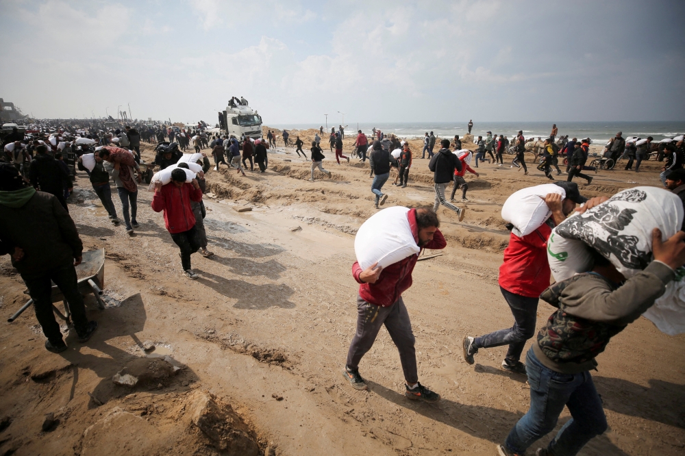Palestinians carry bags of flour they grabbed from an aid truck near an Israeli checkpoint,