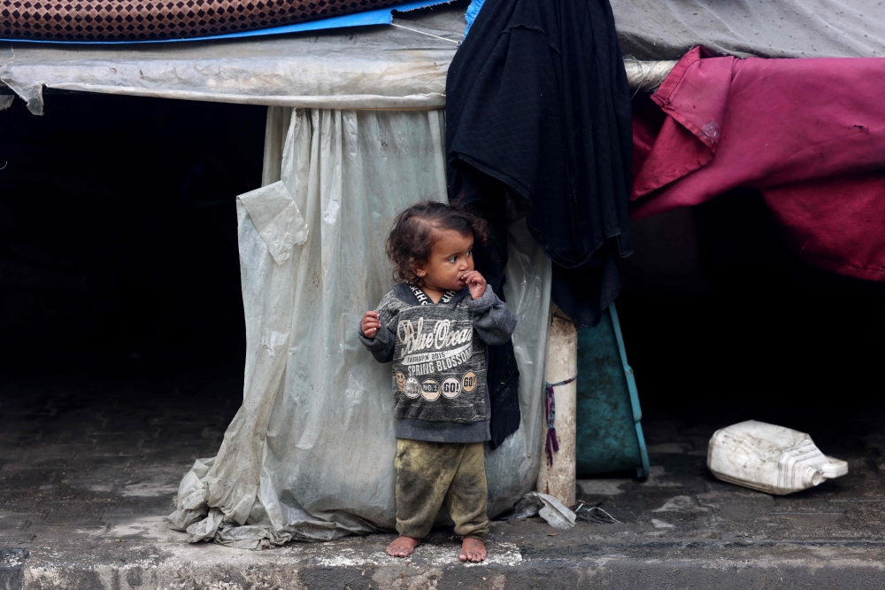 TOPSHOT - A displaced Palestinian child stands outside a makeshift tent attached to a school hosting families from other parts of the Gaza Strip in the Rafah refugee camp in southern Gaza on February 26, 2024, as battles between Israel and the Palestinian militant group Hamas continue for the fifth month.  (Photo by MOHAMMED ABED / AFP)
