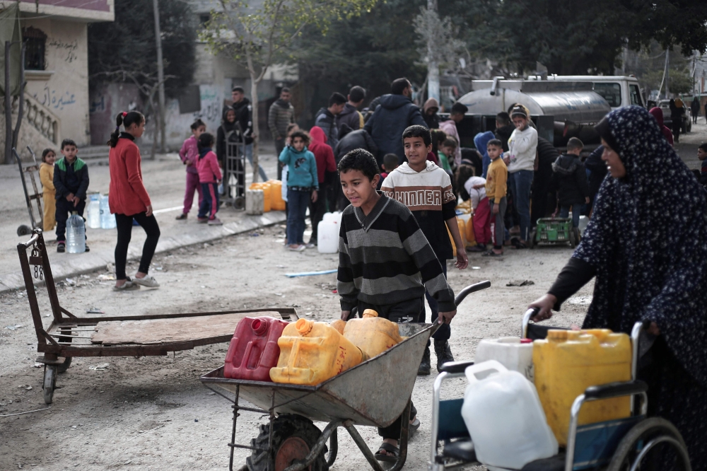 A Palestinian boy pushes a wheelbarrow loaded with water containers at a refugee camp in Rafah. — AFP 