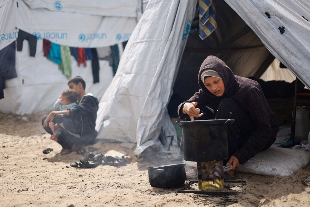 A woman cooks, as displaced Palestinians, who fled their houses due to Israeli strikes shelter in a tent camp, in Rafah