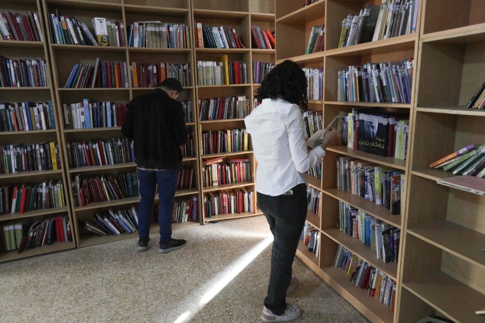 Members of the Kurdistan Centre for Arts and Culture (KCAC), select old books from the shelves before making digital copies, as part of an effort to digitise historic Kurdish volumes and manuscripts, in the northern Iraqi city of Dohuk on February 13, 2024. Many historic documents belonging to Kurds, an ethnic group spread across modern day Iraq, Iran, Syria and Turkey, have been lost or destroyed during their volatile history across the region.  (Photo by Safin HAMID / AFP)

