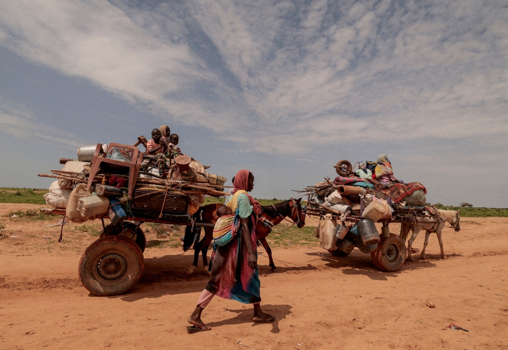 A Sudanese woman, who fled the conflict in Murnei in Sudan's Darfur region, walks beside carts carrying her family belongings upon crossing the border between Sudan and Chad in Adre, Chad. — Reuters file photo