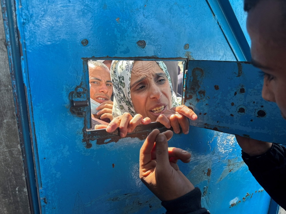 A Palestinian woman speaks with a worker as she waits to receive aid from an UNRWA distribution centre, in Rafah. — Reuters 