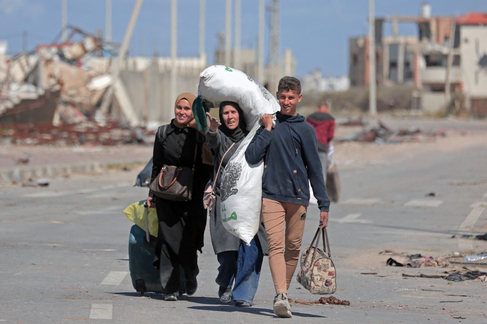 Displaced Palestinians walk along a road near the rubble of houses destroyed by Israeli bombardment at the Nuseirat area in the central Gaza Strip