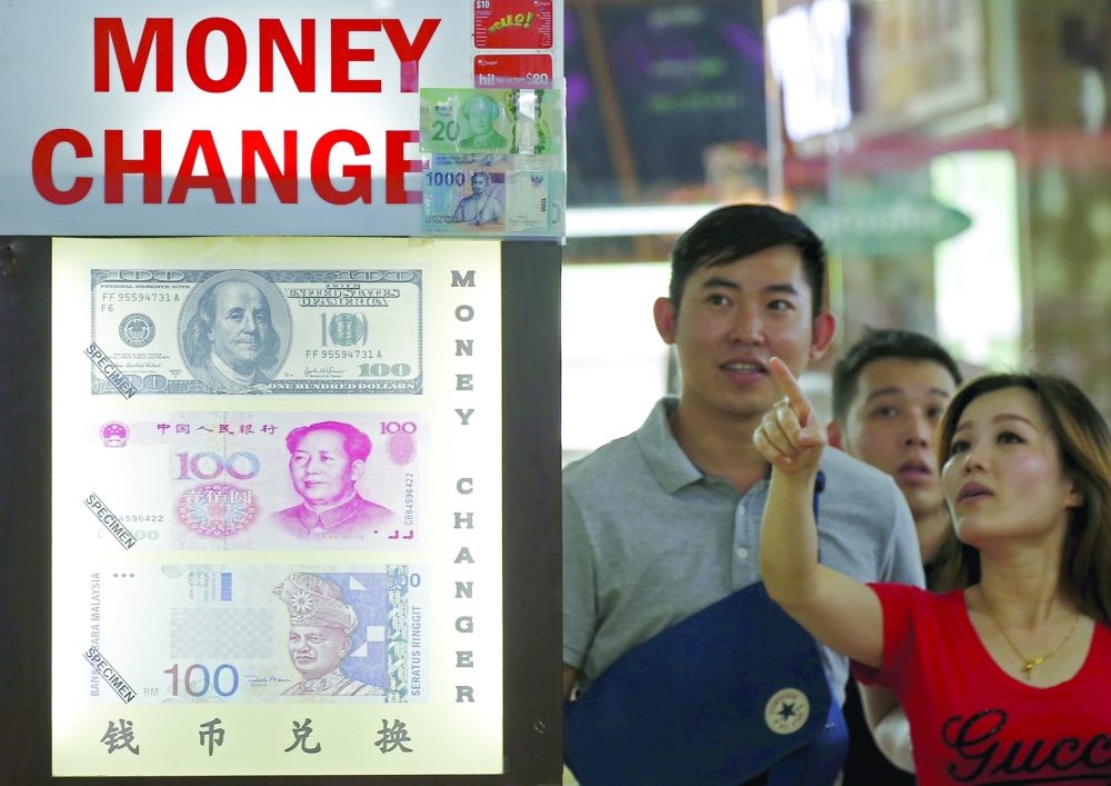 People look at the exchange rate at a money changer displaying posters of US dollars, Chinese yuan and Malaysia ringgit in Singapore. — Reuters