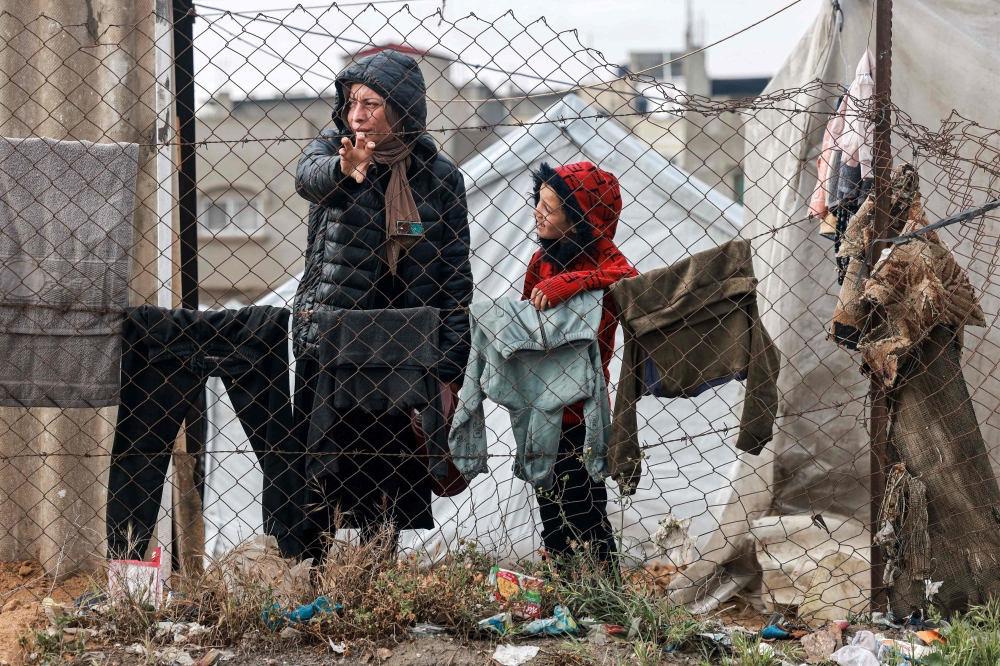 A woman and child stand by drying clothes hanging on a laundry line outside tents housing displaced Palestinians in Rafah