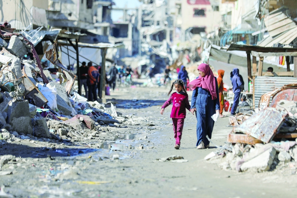 Palestinians walk past the ruins of houses destroyed during Israel's military offensive, in Gaza. — Reuters 