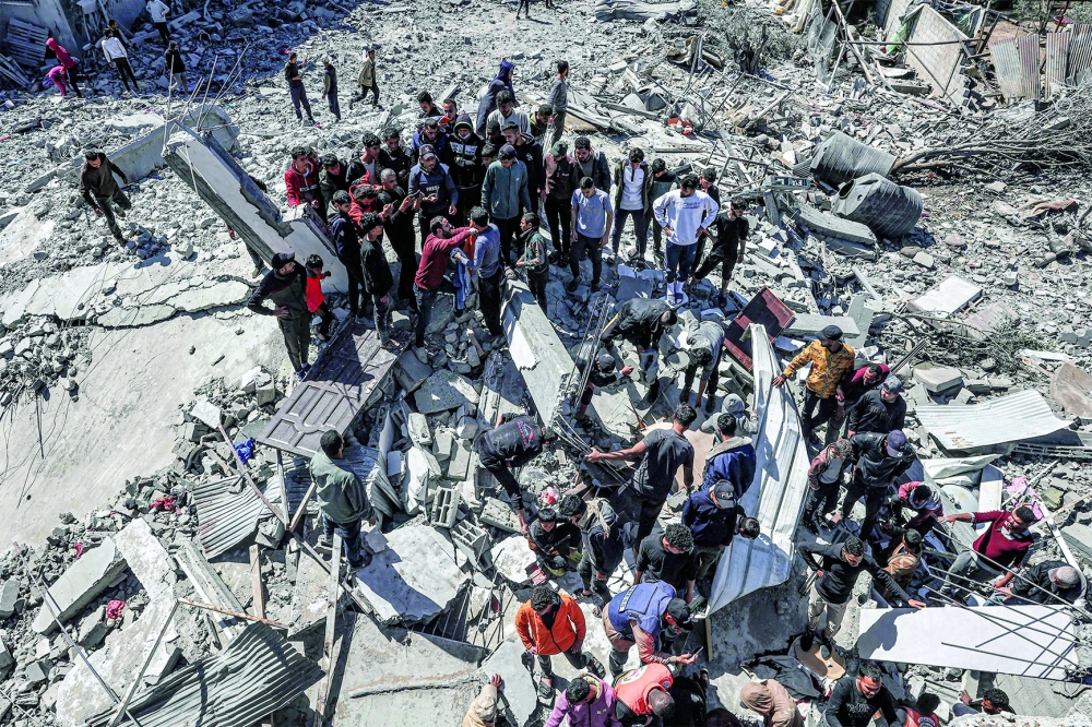 People and first responders inspect the rubble and debris of a building that collapsed following an Israeli air strike in Rafah. — AFP 