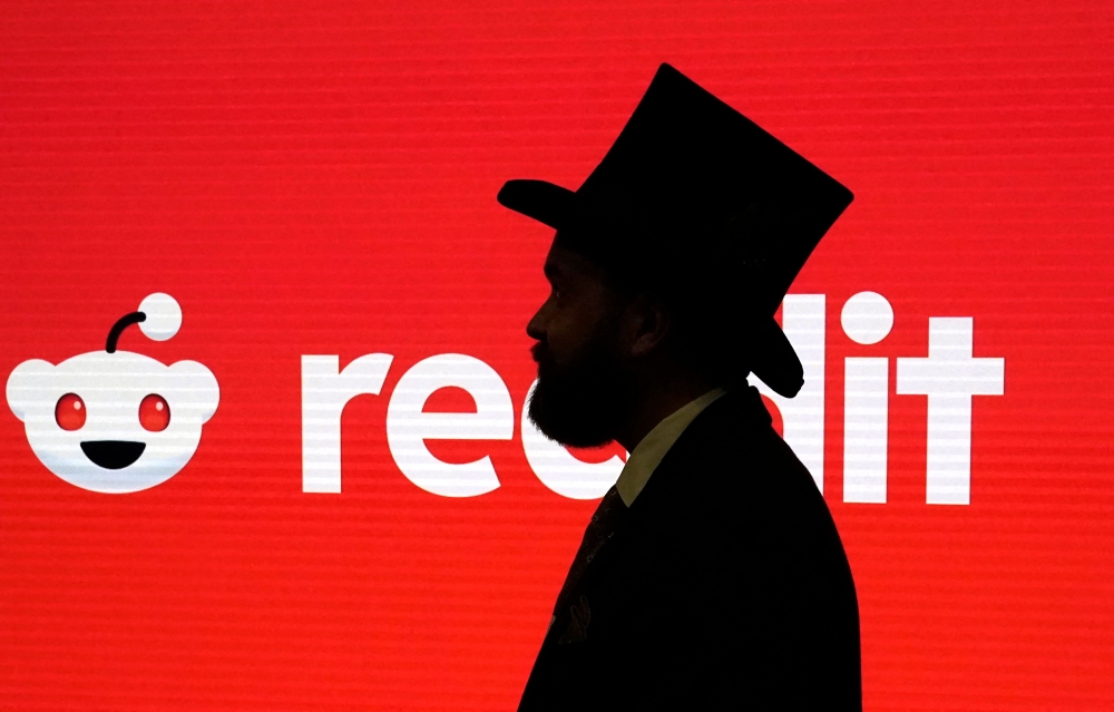 A guest in a top hat before walks pat a Reddit logo before the opening bell as Reddit begins trading on the New York Stock Exchange (NYSE) in New York