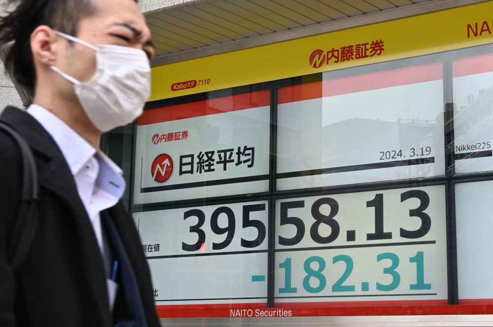 A man walks past an electronic board showing a share price of the Nikkei index of the Tokyo Stock Exchange in Tokyo