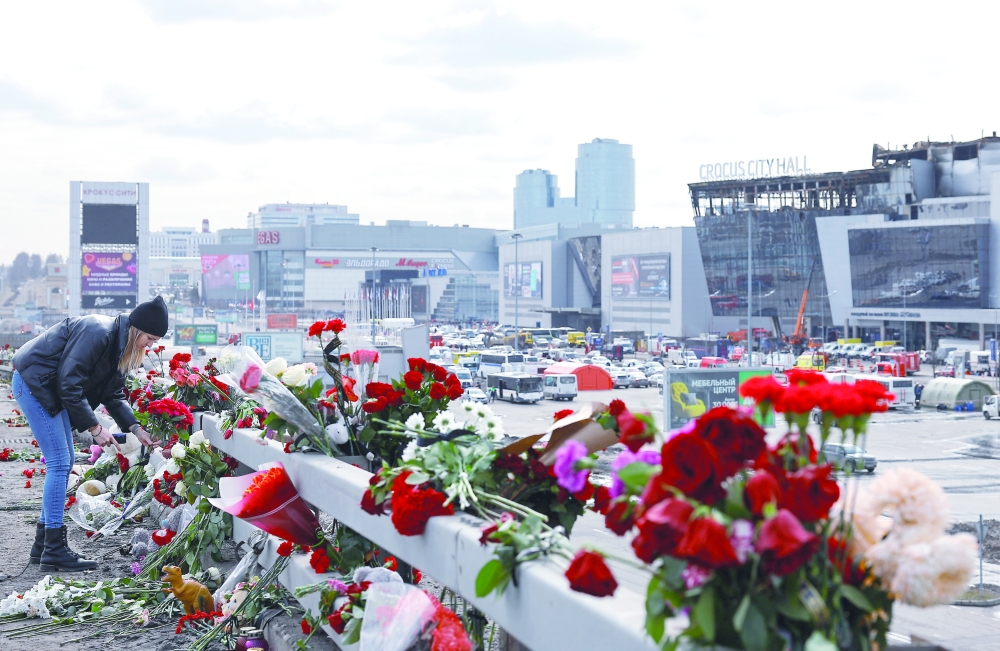A woman lays flowers on the roadside in front of the burnt-out Crocus City Hall, Moscow. — Reuters