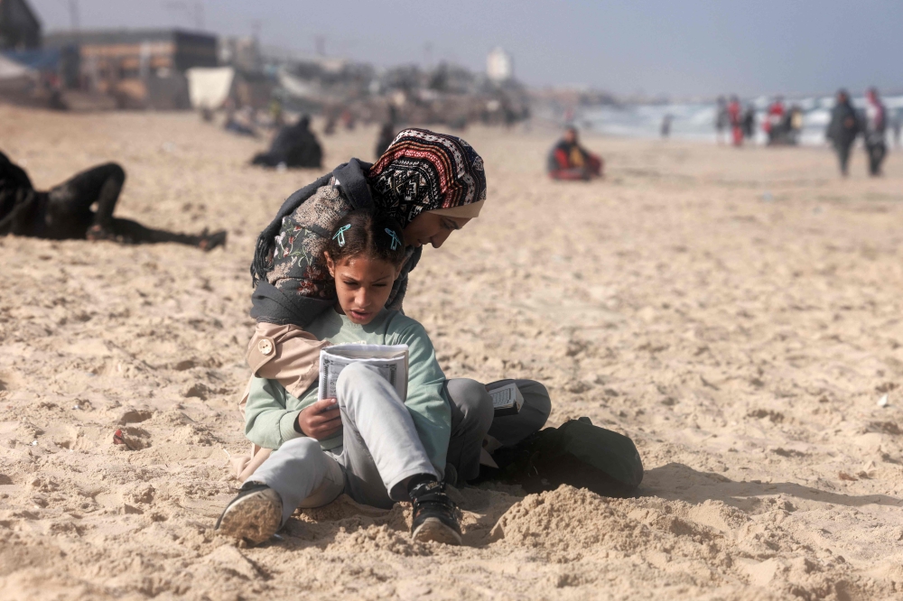 A Palestinian woman and a girl sit along a beach adjoining a makeshift camp for displaced people in Rafah. — AFP 