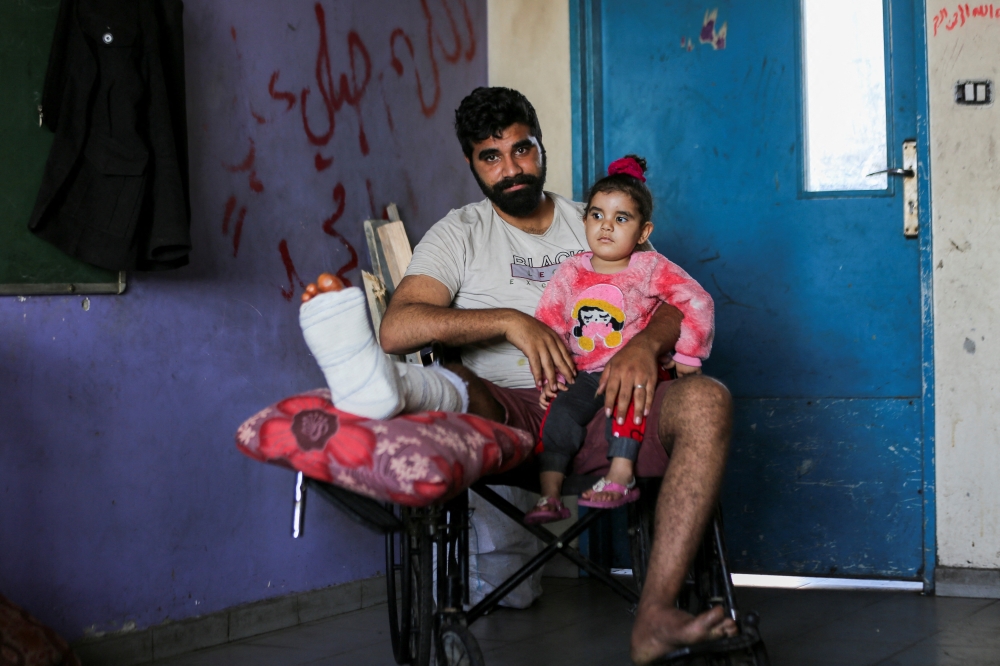 Displaced Palestinian Hamza Abu Alkas, who was wounded while trying to receive aid, holds his daughter as he sits in a classroom at an UNRWA school where they shelter, in Gaza City 