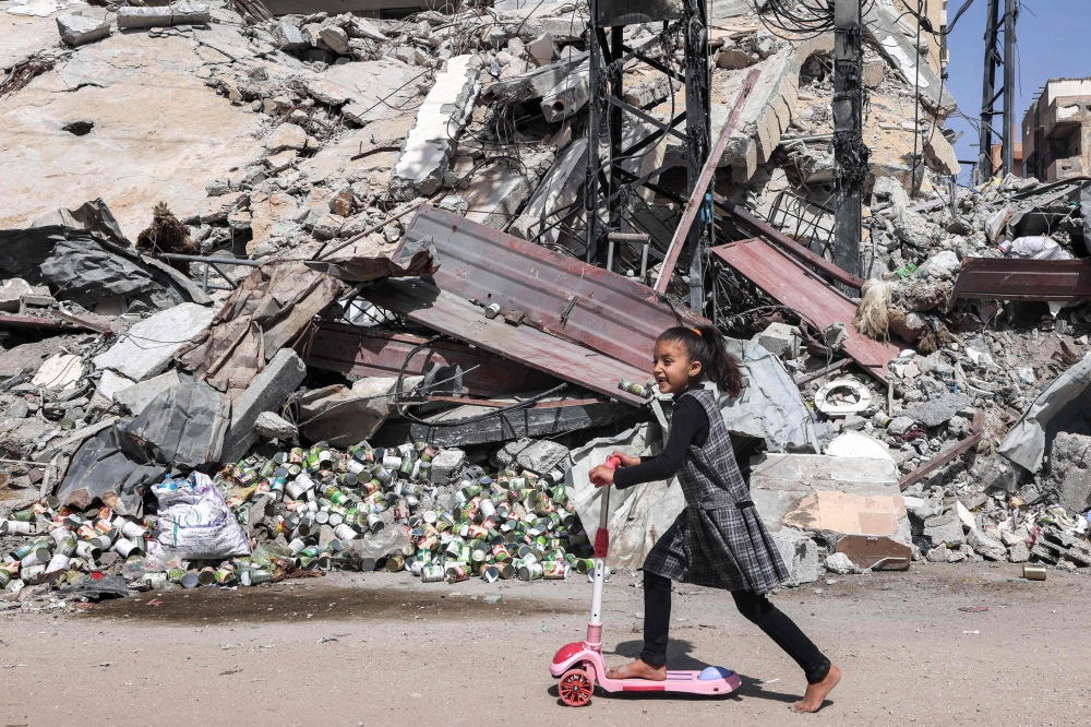 A girl rides a scooter past the rubble of a destroyed building in Rafah in the southern Gaza Strip amid the ongoing conflict in the Palestinian territory between Israel and Hamas. - AFP


