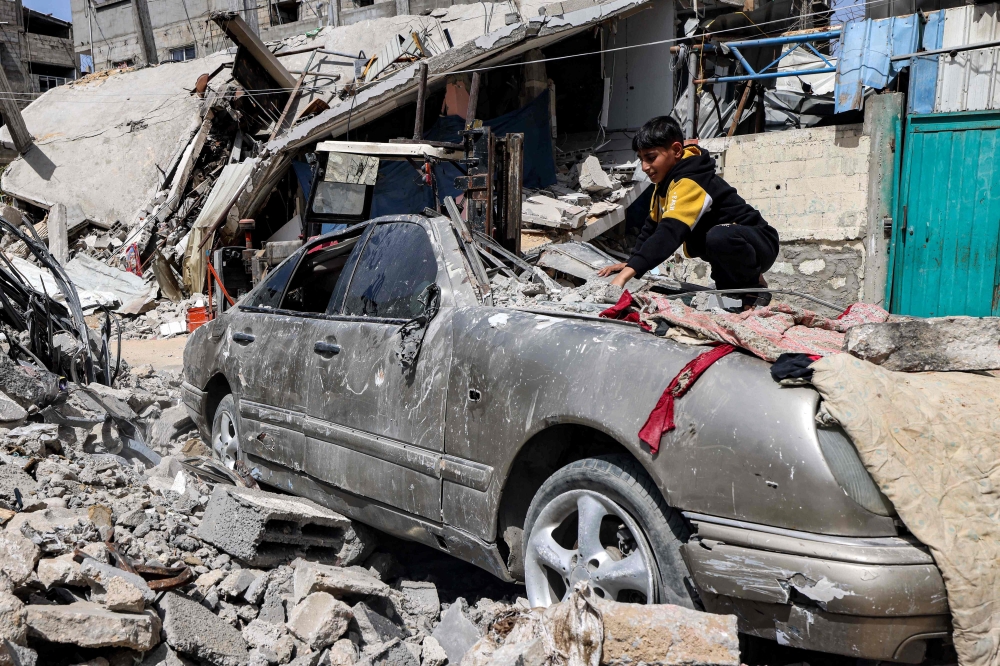 A boy clears rubble from atop a heavily damaged vehicle outside a destroyed building in Rafah on Friday. — AFP 

