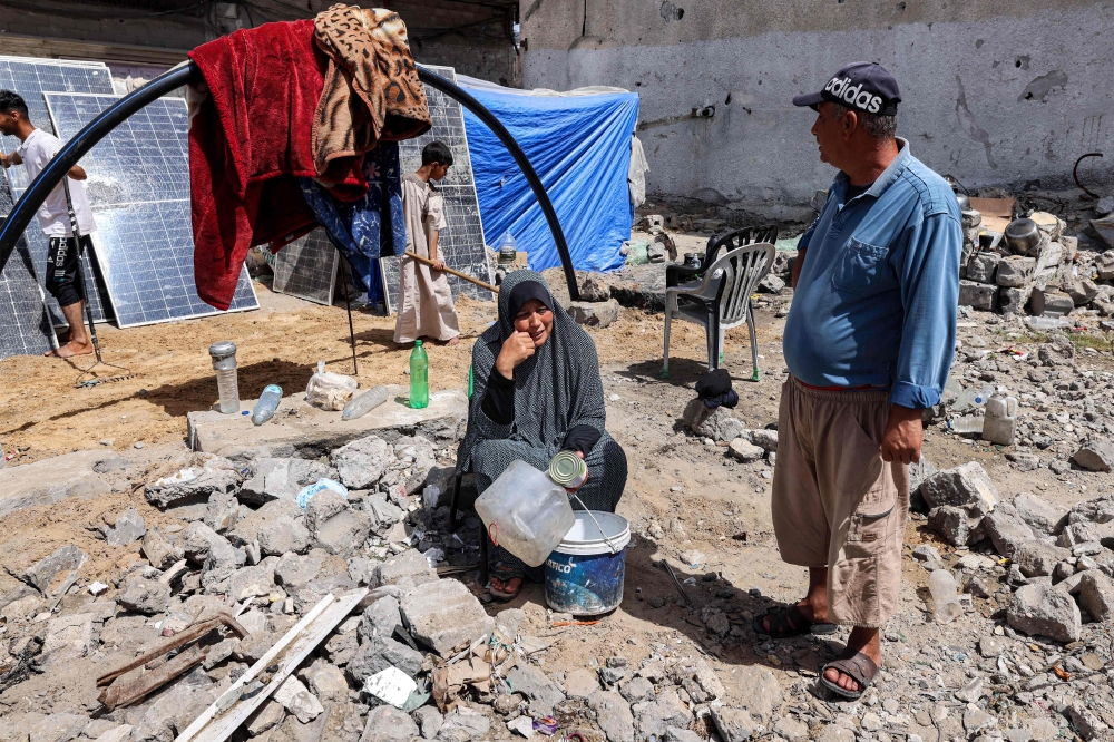 A woman sits holding empty containers outside a tent pitched by a destroyed building in Rafah. — AFP 