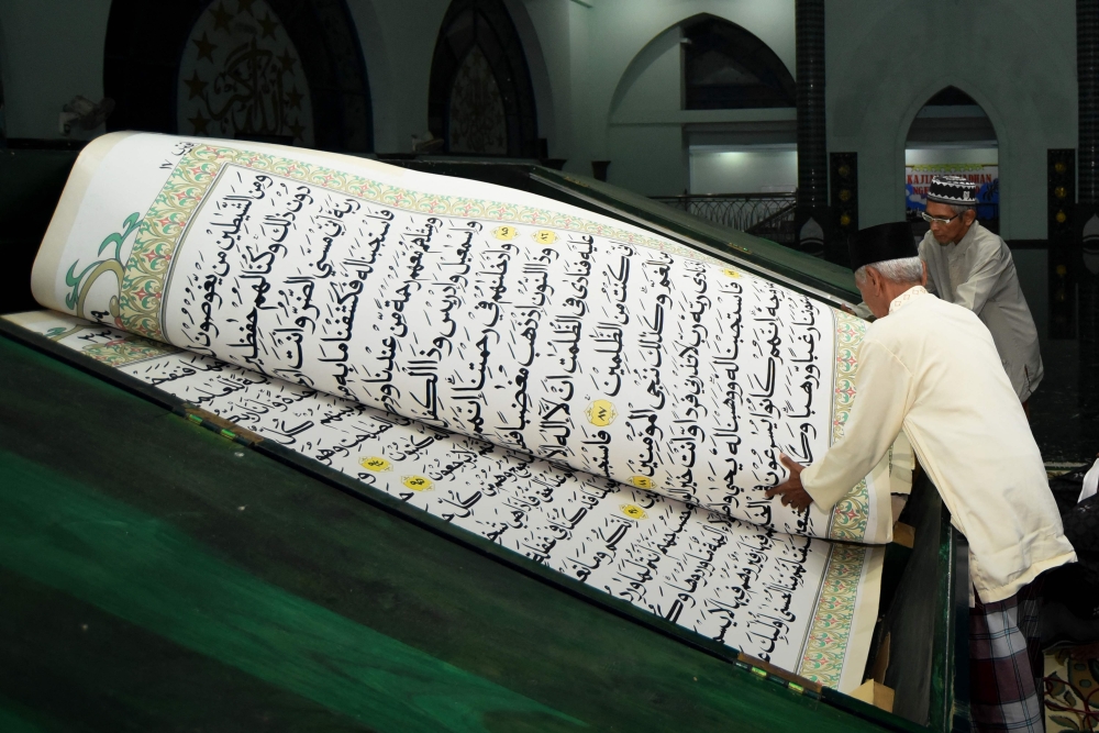 People read a giant handwritten copy of Holy Quran, measuring  142 x 210 centimetre, during the holy month of Ramadhan, at the Baiturrahman Mosque in Banyuwangi, East Java, on Wednesday. — AFP 