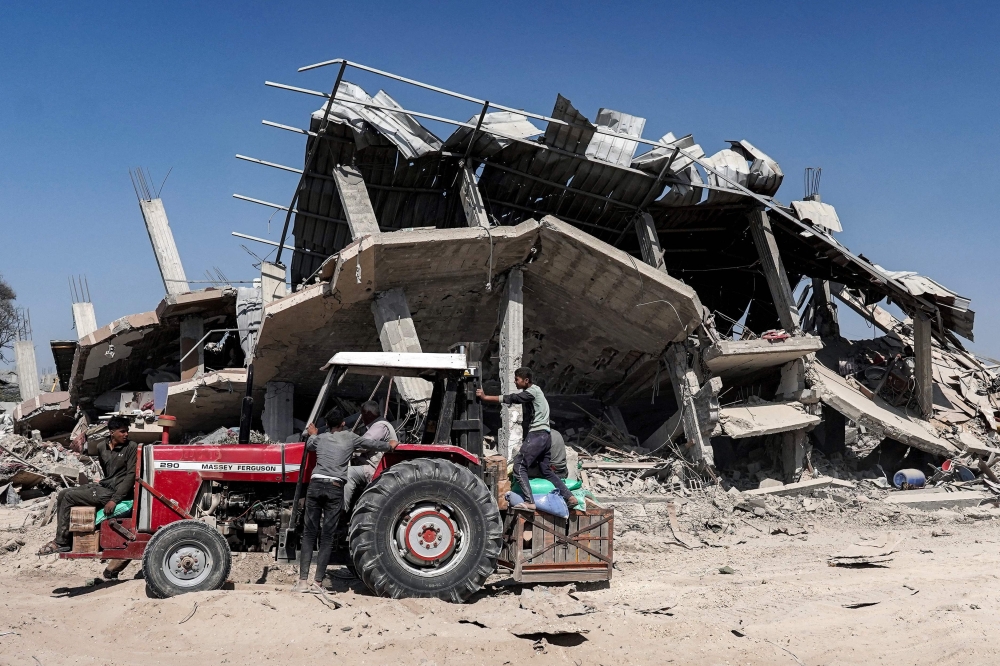 People ride on a tractor picking up salvaged items from a damaged building in Khan Yunis 