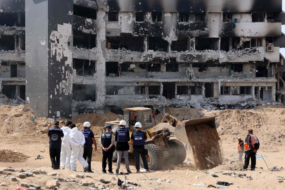 TOPSHOT - A United Nations (UN) team visit as Palestinian civil defence recover human remains the grounds of Al-Shifa hospital, Gaza's largest hospital, which was reduced to ruins by a two-week Israeli raid, on April 8, 2024, amid the ongoing conflict between Israel and the Palestinian Hamas militant group.
  (Photo by AFP)