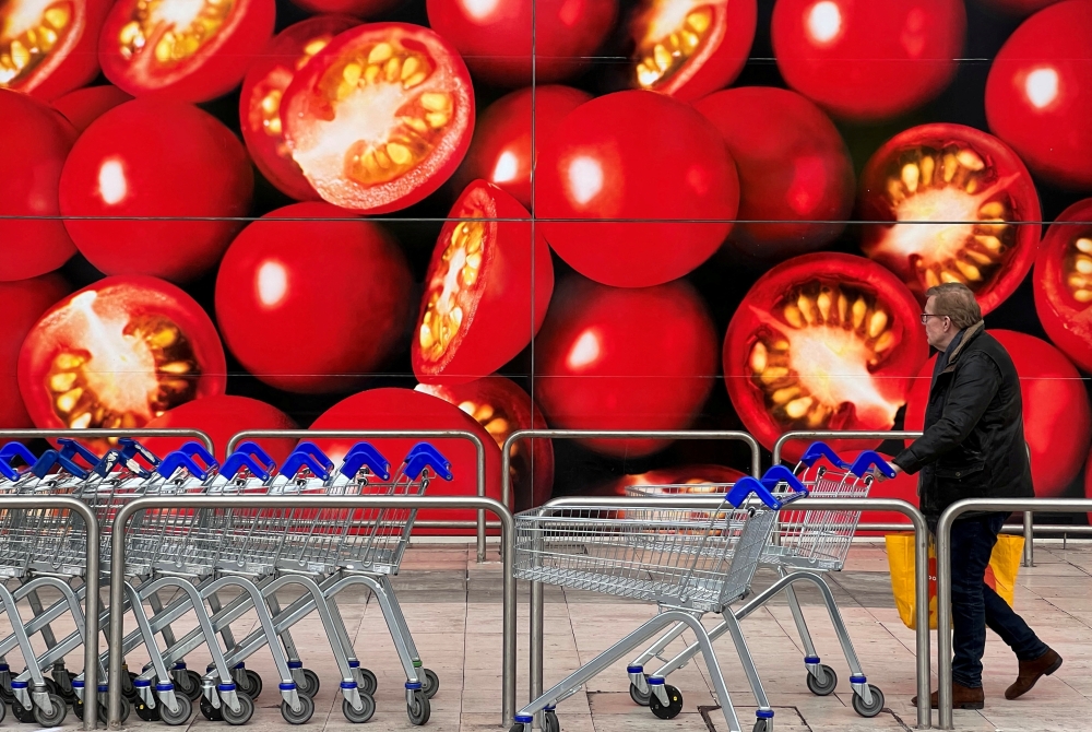 A shopper walks next to a photographic depiction of tomatoes on a Tesco supermarket in London. — Reuters