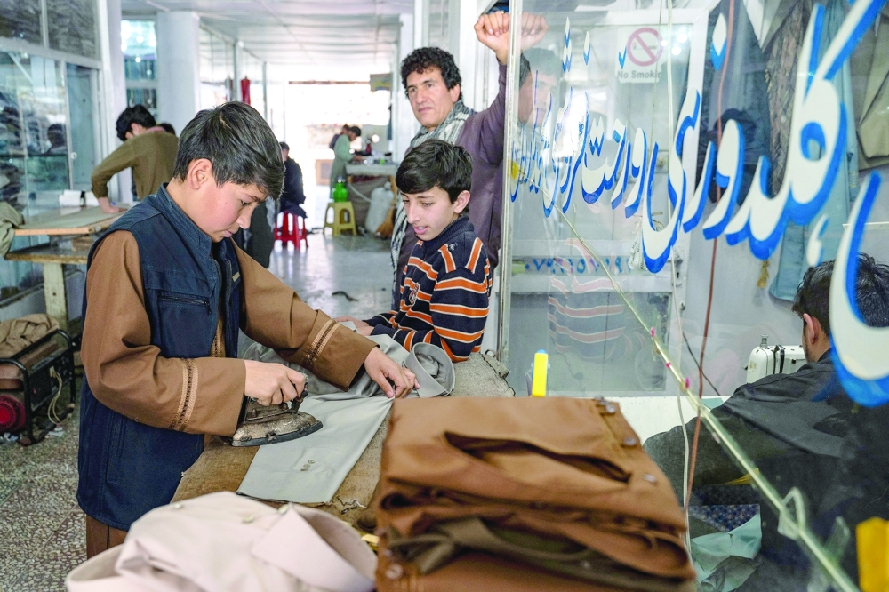 An Afghan youth (L) irons clothes ahead of Eid al-Fitr, which marks the end of the Muslim holy fasting month of Ramadan at a tailor workshop in Kabul on April 7, 2024.